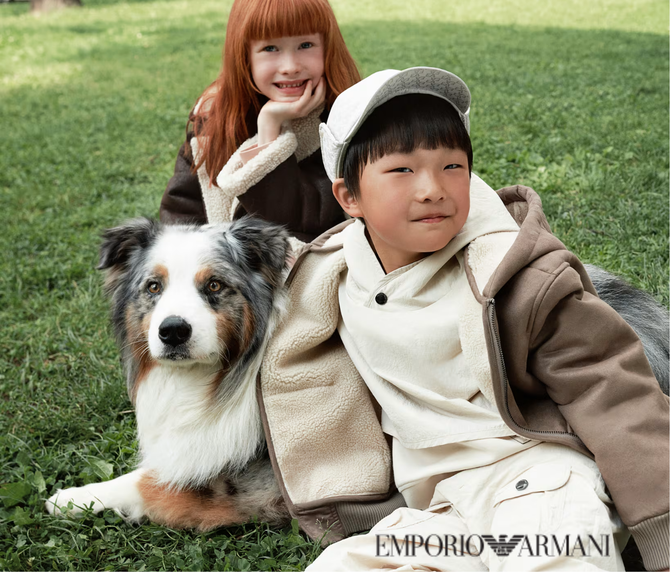 Two children and a dog sitting on grass, with 'Emporio Armani' branding visible.